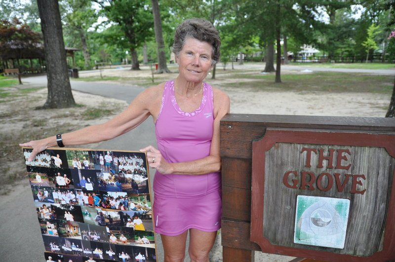 Doris Hicks, president of the Grove Park Running Club, stands at the entrance to the park with a board full of photos of the club's events through the years. BY NICK ROTH
