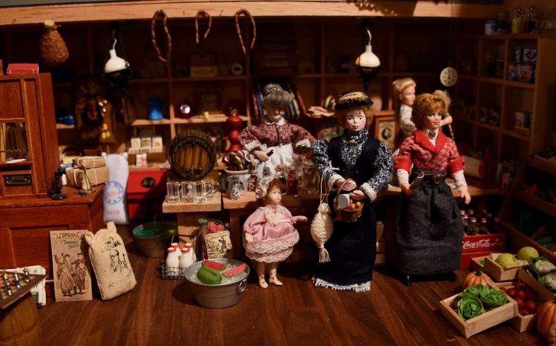 Doll shoppers, in handmade dresses, are displayed in a turn-of-the century general store.