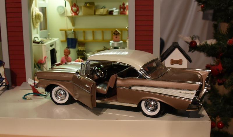 A vintage model Chevrolet Bel Air sits outside a miniature garage.