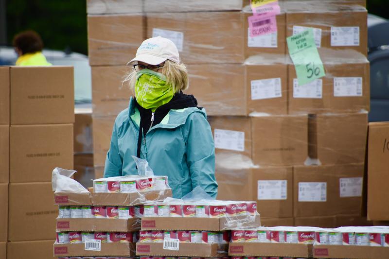 Looking out from behind a face covering, a volunteer stands ready to load canned goods.