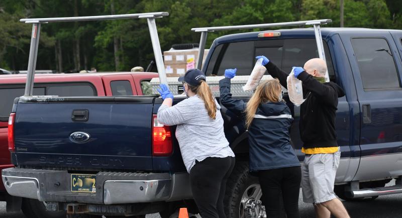 Three volunteers reach over the bed of a truck to load food.