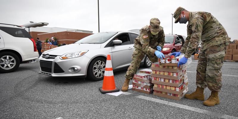 Two Delaware Army National Guard members cut open boxes of canned goods.