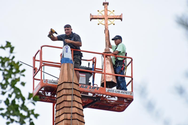 Andrew Lewandowski, left, drills a hole into the steeple as Gerardo Hernandez holds on tight to the new cross.