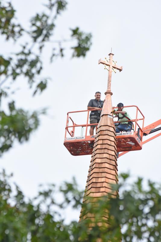 Andrew Lewandowski, left, and Gerardo Hernandez of Bayside Exteriors secure the new cross to the steeple.