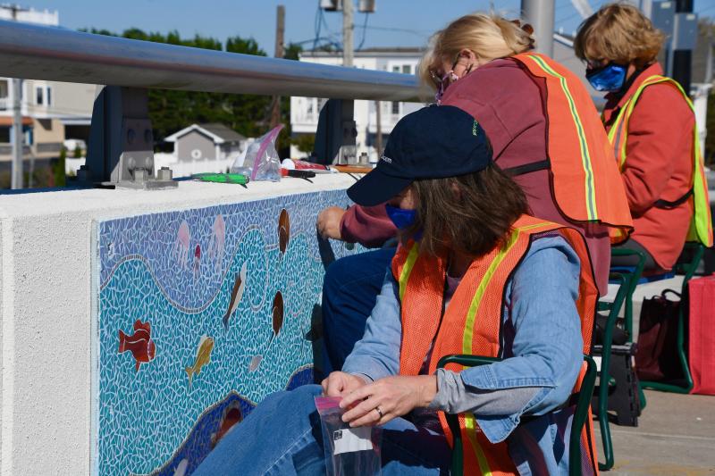 Volunteers (l-r) Mary Pasi, Lisa Sutcliffe and Sue Sandmeyer, project chairwoman, work to cover the seams on the 2-by-5-foot panels. Fifty feet of artwork will be displayed on each side of the bridge.