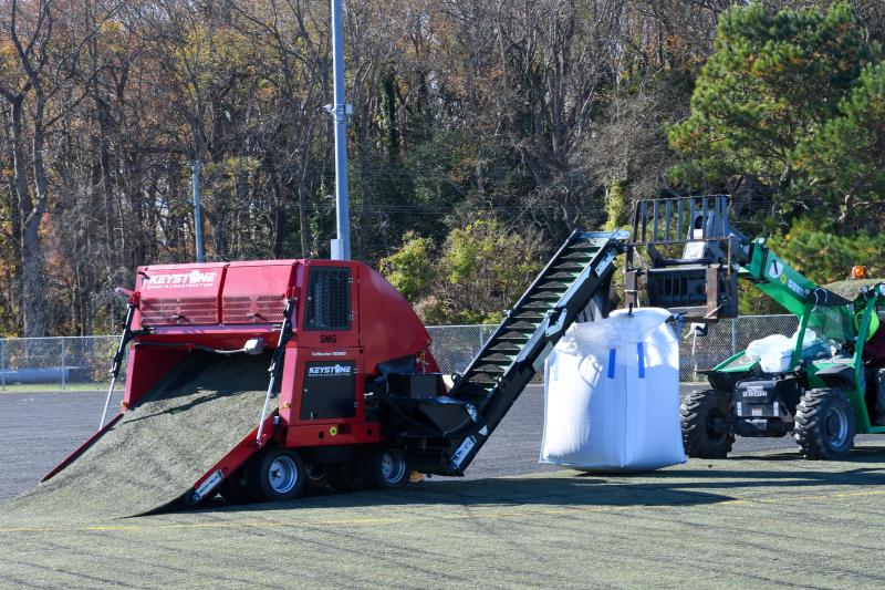 The red machine snatches and rolls up the carpet while black runner pellets are dumped into a bag. All materials will be recycled.
