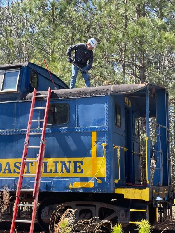 After climbing a ladder, volunteer Paul Moore does important work to secure the caboose’s roof.