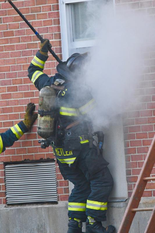 A firefighter uses a pry bar to open a window to gain access to a smoke-filled room to search for people inside during an Aug. 9 training session.