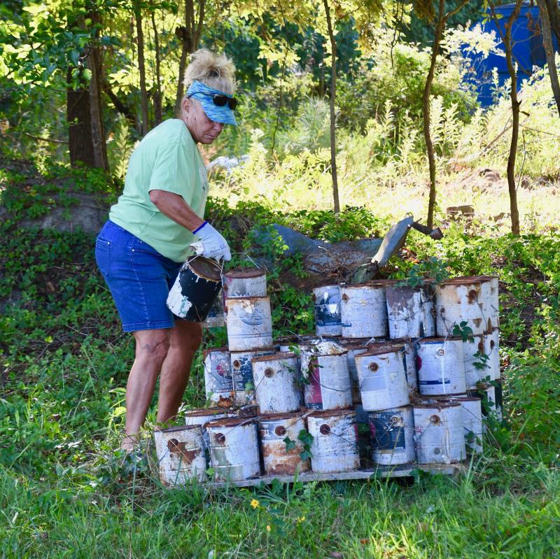 Jo Milbut starts moving cans of old paint from a large pile as Dogfish Head employees help clear the site for a homeless village.