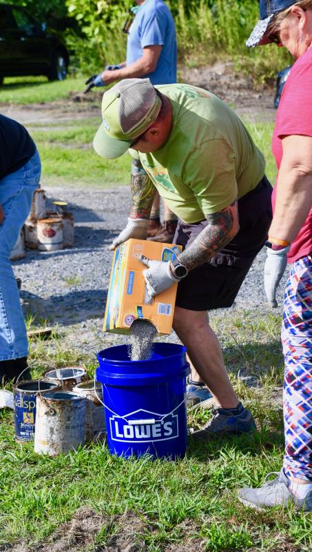 Tony Milbut pours kitty litter into a half-full, 5-gallon bucket of old paint.