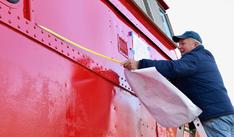 Lewes Junction Railroad & Bridge Association board member David Ludlow measures to find the center before a Pennsylvania Railroad logo is applied to the caboose.