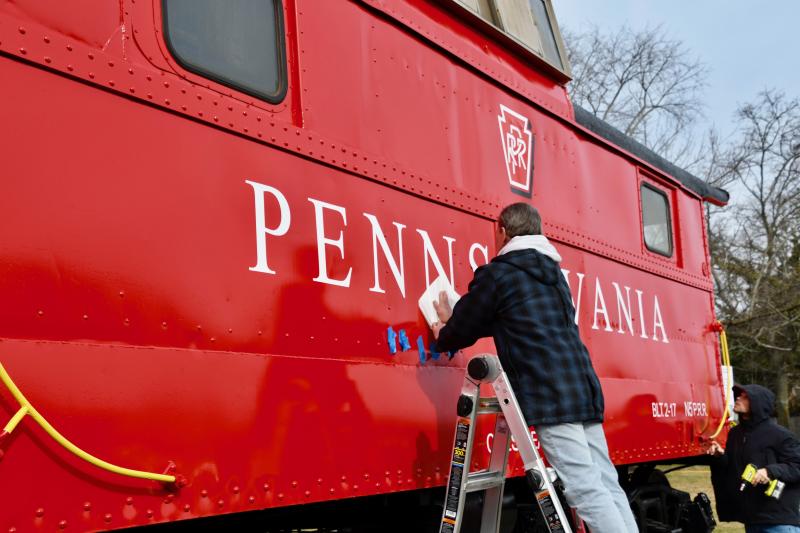 D.J. Baker of Southern Delaware Signs removes the last piece of stencil paper during a lettering project Jan. 10 on the restored 1917 Pennsylvania Railroad caboose adjacent to the Lewes Public Library. RON MACARTHUR PHOTOS