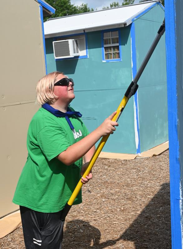 Ayden Beavers reaches up high with a roller extension to apply paint to the side of a shelter.