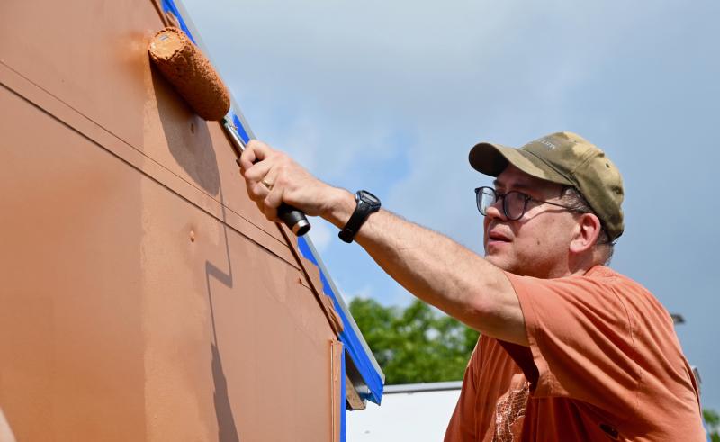 Tom Batchik of Columbia, Md., reaches high to paint near the roof of a Pallet shelter.