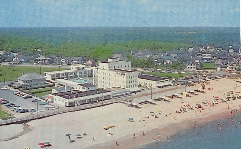 In this aerial image, the Henlopen Motor Lodge is located behind the Henlopen Hotel, with a pool in between.