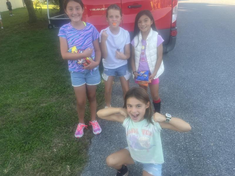 Offering water and candy are in back (l-r) Lena Torres, Ella Tyndall and Malee Burke. Evan Chubb is kneeling showing off her guns. They are students at Milton Elementary School who were helping the Mariner Middle School PTO raise money by selling snacks.