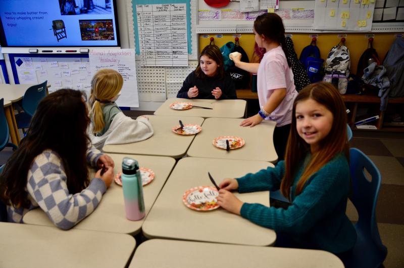 Adelynn Rios smiles at the camera while Khloey Hill-West shakes the solidifying butter for Chloe Shugarbean to hear.