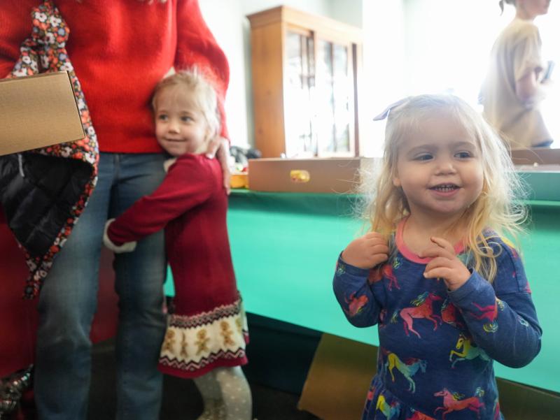 Leitner sisters Willa, 4, left, and Virginia, 2, smile by their mother at the Trees of Cheer event.