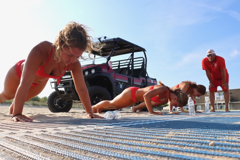 Pushups are part of the rookie lifeguard competition. Shown are (l-r) Sarah Bieler, Savannah Couch and Marlise Harris, under the watchful eye of Beach Patrol Capt. Strohm Edwards. BILL SHULL PHOTOS