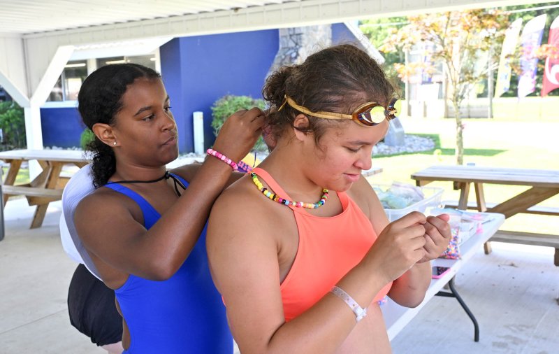 Counselor Jo’Mara Drummond, left, assists athlete Armani Jackson with putting on her handmade necklace.
