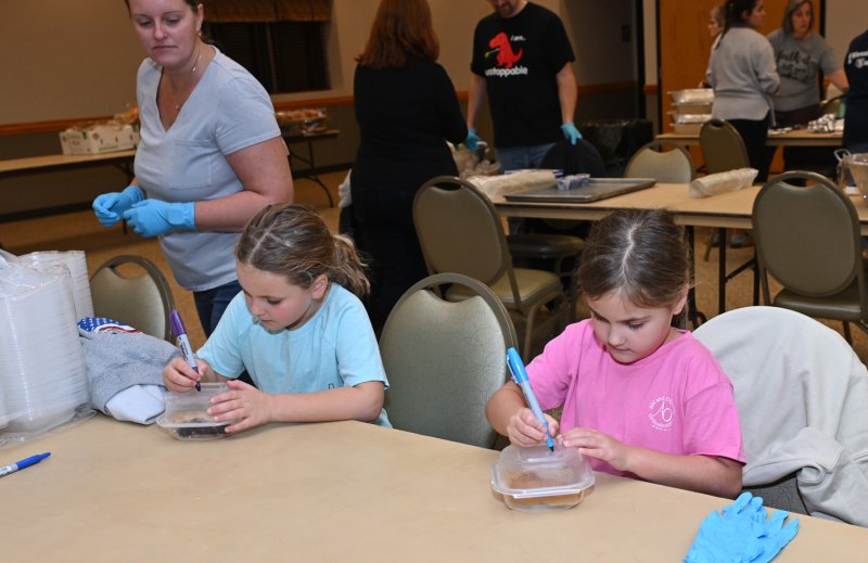 Kinley Streett, left, and Lucy Taylor write the type of pie in the dessert package as Stacie Baker Streett looks on.