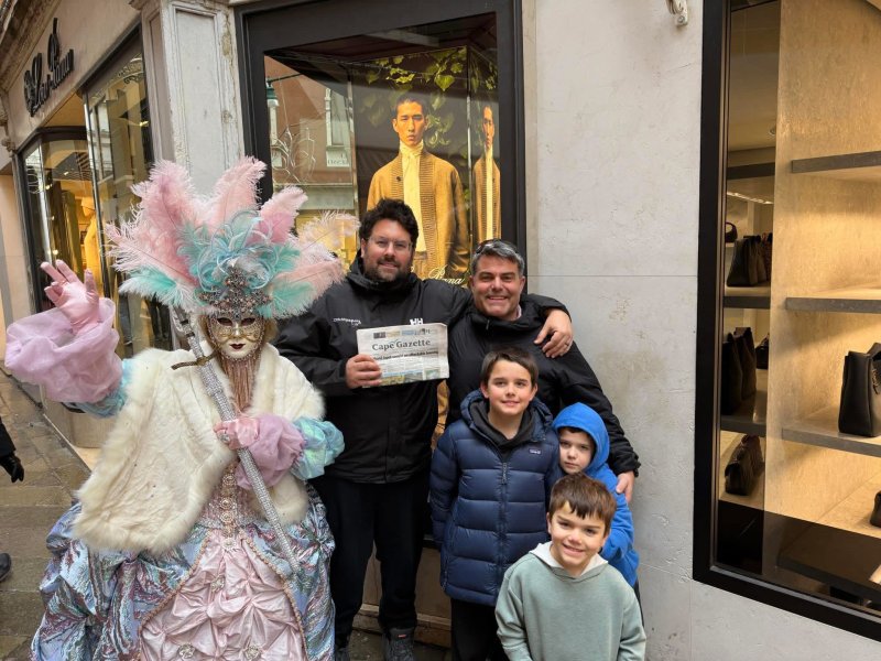 A Venetian masquerader and (l-r) Jamin Hudson of Lewes and Jason Johnson of Milton pose for a picture with Hudson’s sons Henry, Leo and Alexander, and a copy of the Cape Gazette in Venice, Italy, while attending the 2026 Winter Olympics. SUBMITTED PHOTO