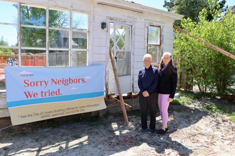 Neil Shister, left, and Cait Clarke stand next to the banner they hung in front of their home at 311 Park Ave. in Lewes. Only the front wall remains of the 1950-vintage structure. The couple is battling the city over a permit for the job. They claim they are following the permit the city issued for renovations, but city building official Jon Ward has determined they now need a demolition permit. Ward has placed a partial stop-work order on the project. Clarke and Shister have a hearing before the city’s board of adjustment Tuesday, May 5. BILL SHULL PHOTOS